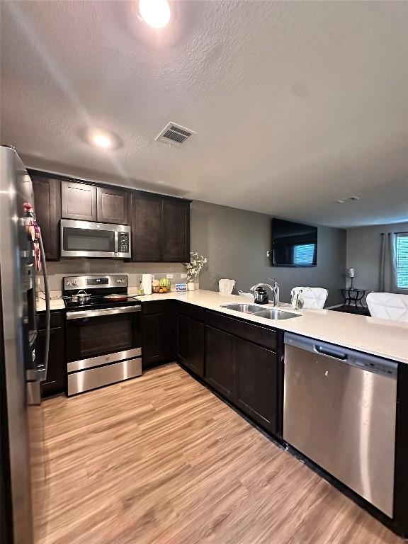 1214 Smallmouth Rd, Bastrop, TX 78602 - kitchen with stainless steel appliances, light wood finished floors, light countertops, dark brown cabinetry, and a textured ceiling