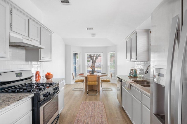9273 Vigen Cir, Austin, TX 78748 - kitchen with stainless steel appliances, under cabinet range hood, light wood-style flooring, tasteful backsplash, and light stone countertops