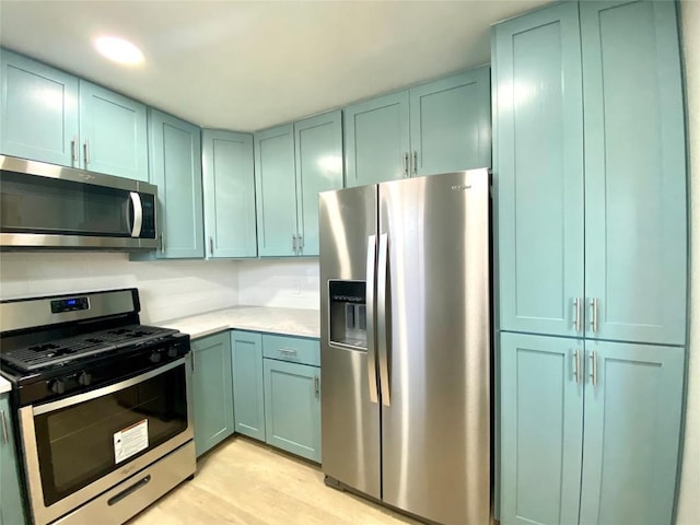 6920 Bethune Ave, Austin, TX 78752 - kitchen featuring appliances with stainless steel finishes, light countertops, light wood finished floors, and blue cabinets