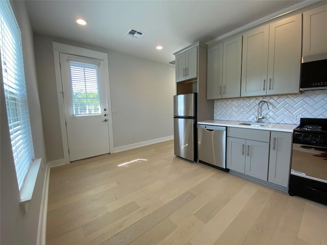 6920 Bethune Ave, Austin, TX 78752 - kitchen with stainless steel appliances, gray cabinetry, tasteful backsplash, light countertops, and light wood-type flooring