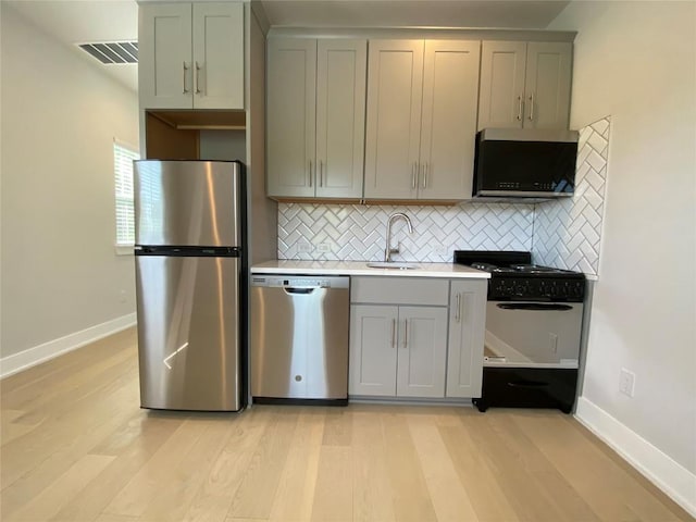 6920 Bethune Ave, Austin, TX 78752 - kitchen with stainless steel appliances, gray cabinetry, light wood-style floors, tasteful backsplash, and light countertops