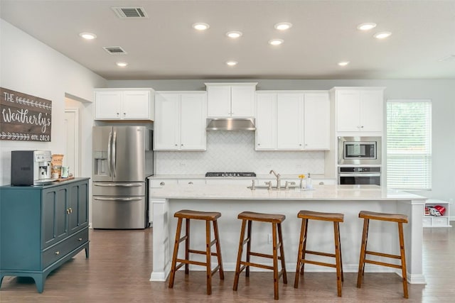 2049 Cartway Ct, Leander, TX 78641 - kitchen with stainless steel appliances, under cabinet range hood, white cabinetry, tasteful backsplash, and a center island with sink