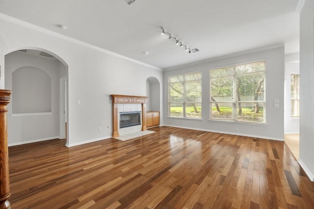 3213 Summer Canyon Dr, Austin, TX 78732 - unfurnished living room featuring wood finished floors, rail lighting, a tile fireplace, ornamental molding, and arched walkways