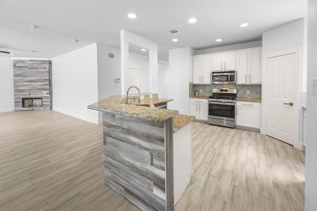 8104 Broken Branch Dr, Round Rock, TX 78681 - kitchen with appliances with stainless steel finishes, light wood-style floors, open floor plan, white cabinets, and a tiled fireplace