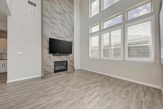 600 E Baylee Love Ln, Austin, TX 78717 - unfurnished living room with light wood-type flooring, a tile fireplace, and a high ceiling