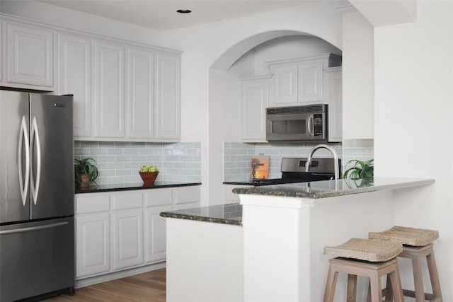 3406 Menchaca Rd Unit 14, Austin, TX 78704 - kitchen featuring stainless steel appliances, a breakfast bar, dark stone counters, white cabinets, and arched walkways