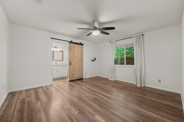 7604 Beinville Cv, Austin, TX 78749 - unfurnished bedroom with a barn door, wood finished floors, ensuite bath, and a ceiling fan