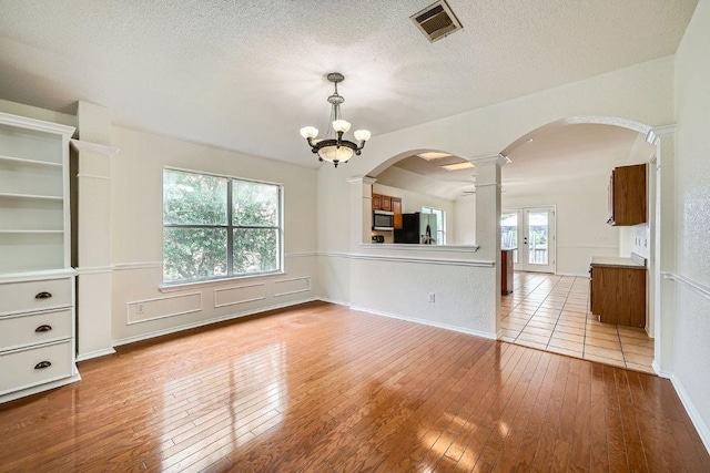 1506 Willow Bluff Dr, Pflugerville, TX 78660 - unfurnished room featuring decorative columns, arched walkways, hardwood / wood-style floors, a textured ceiling, and a chandelier