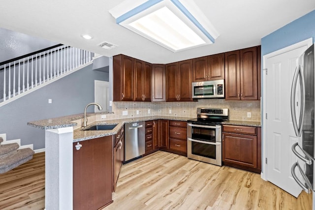 9105 Trickle Trace Trl, Round Rock, TX 78681 - kitchen with appliances with stainless steel finishes, a peninsula, light wood-type flooring, light stone countertops, and tasteful backsplash
