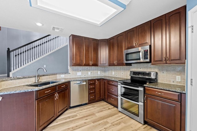 9105 Trickle Trace Trl, Round Rock, TX 78681 - kitchen featuring appliances with stainless steel finishes, light stone counters, light wood-style floors, a peninsula, and tasteful backsplash