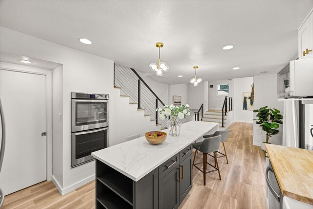 3704 Laurel Ledge Ln, Austin, TX 78731 - kitchen featuring stainless steel double oven, open shelves, a center island, light wood-type flooring, and decorative light fixtures