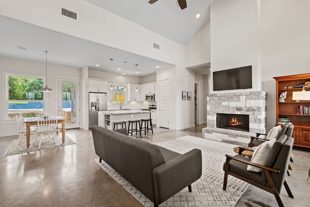 503 Alva Dr, Spicewood, TX 78669 - living area featuring a ceiling fan, a stone fireplace, healthy amount of natural light, a towering ceiling, and concrete floors