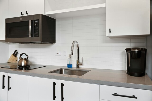 49 Navasota St Unit 216, Austin, TX 78702 - kitchen with stainless steel microwave, backsplash, white cabinetry, and black electric stovetop