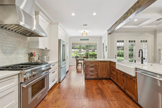 128 Squires Dr, Lakeway, TX 78734 - kitchen with high quality appliances, wall chimney exhaust hood, crown molding, hardwood / wood-style floors, and light countertops