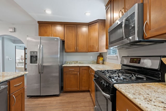 1101 Mahan Dr, Austin, TX 78721 - kitchen with stainless steel appliances, arched walkways, light wood finished floors, brown cabinets, and recessed lighting