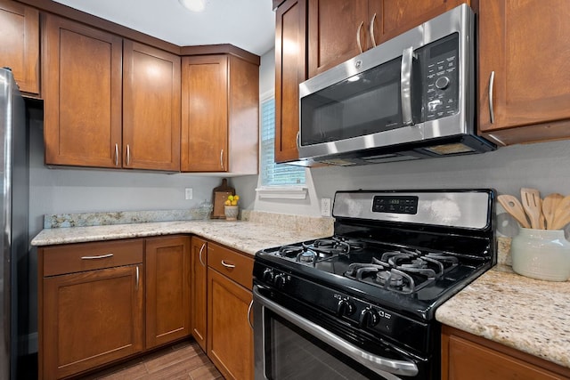 1101 Mahan Dr, Austin, TX 78721 - kitchen with appliances with stainless steel finishes, light wood-type flooring, brown cabinets, and light stone counters