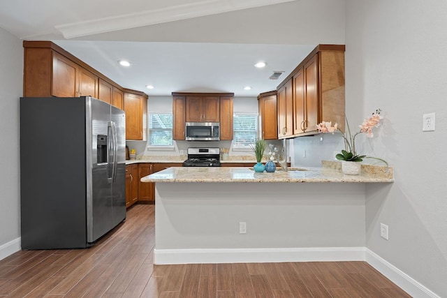 1101 Mahan Dr, Austin, TX 78721 - kitchen with appliances with stainless steel finishes, a peninsula, wood finished floors, brown cabinetry, and recessed lighting