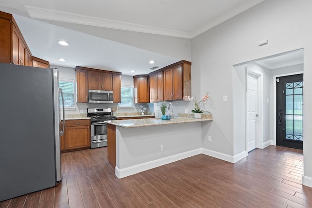 1101 Mahan Dr, Austin, TX 78721 - kitchen featuring stainless steel appliances, a peninsula, dark wood finished floors, ornamental molding, and light stone countertops