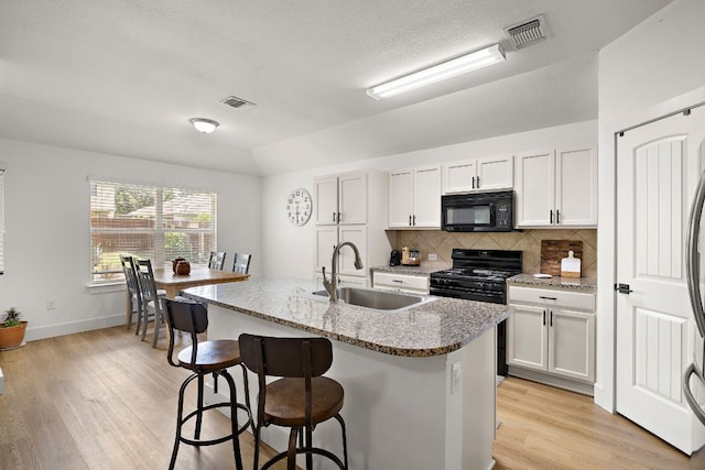 413 Luna Vista Dr, Hutto, TX 78634 - kitchen featuring black appliances, decorative backsplash, a kitchen bar, light wood-type flooring, and a center island with sink