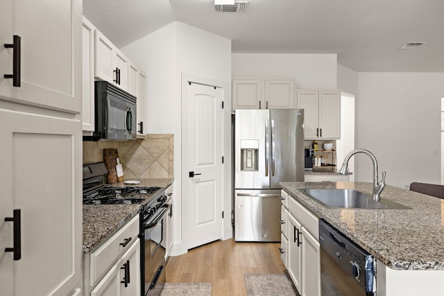 413 Luna Vista Dr, Hutto, TX 78634 - kitchen featuring black appliances, light wood-style flooring, a kitchen island with sink, and stone counters
