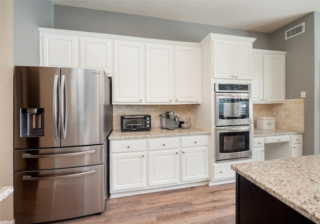 401 Kimra Cv, Georgetown, TX 78628 - kitchen featuring stainless steel appliances, white cabinetry, decorative backsplash, and light wood-style flooring