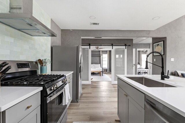 4911 Brighton Rd, Austin, TX 78745 - kitchen featuring appliances with stainless steel finishes, a barn door, wall chimney range hood, light wood-type flooring, and light countertops