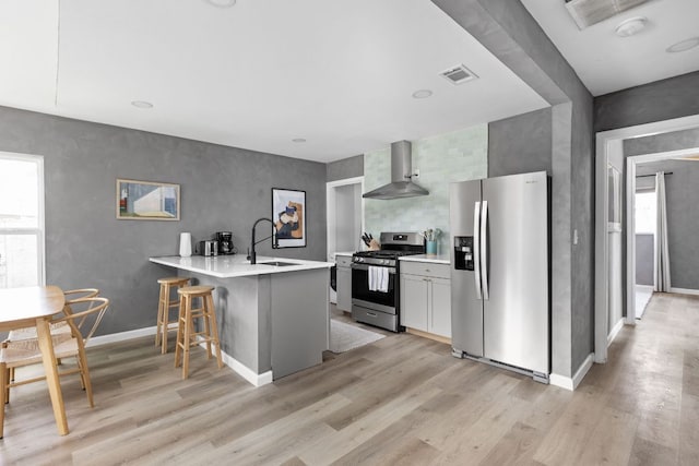 4911 Brighton Rd, Austin, TX 78745 - kitchen with stainless steel appliances, wall chimney range hood, a peninsula, and light wood-style flooring