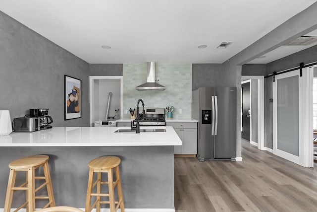 4911 Brighton Rd, Austin, TX 78745 - kitchen with appliances with stainless steel finishes, wall chimney exhaust hood, light wood-type flooring, a barn door, and a kitchen bar