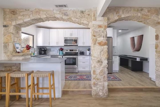 17708 Cherry Ln, Lago Vista, TX 78645 - kitchen with stainless steel appliances, white cabinetry, a breakfast bar area, light wood-style floors, and a peninsula