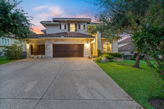 mediterranean / spanish-style home with a tile roof, driveway, a yard, stone siding, and a garage