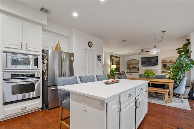 kitchen featuring appliances with stainless steel finishes, white cabinets, a kitchen bar, a center island, and dark wood-style floors