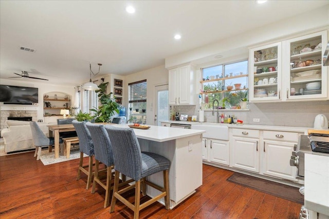 kitchen featuring light countertops, white cabinetry, a kitchen bar, tasteful backsplash, and glass insert cabinets