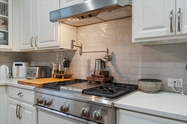 kitchen with ventilation hood, white cabinetry, light countertops, and decorative backsplash