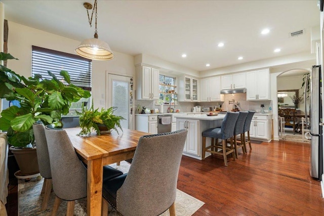 dining space featuring arched walkways, recessed lighting, and dark wood finished floors