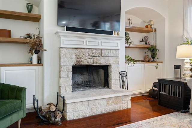 living area featuring dark wood-style floors and a stone fireplace
