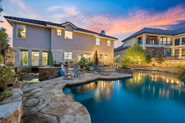 pool at dusk with a patio area, an outdoor kitchen, and an outdoor pool