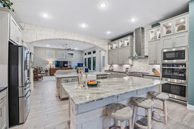 4644 Arques Ave, Round Rock, TX 78681 - kitchen with appliances with stainless steel finishes, wall chimney range hood, a center island with sink, arched walkways, and ceiling fan