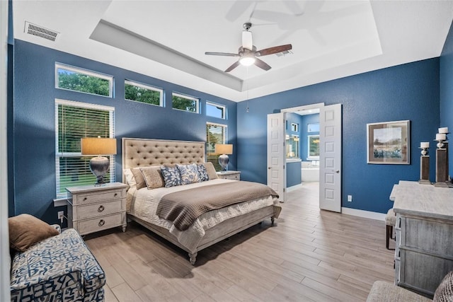 4644 Arques Ave, Round Rock, TX 78681 - bedroom featuring a raised ceiling, light wood-style flooring, multiple windows, and connected bathroom