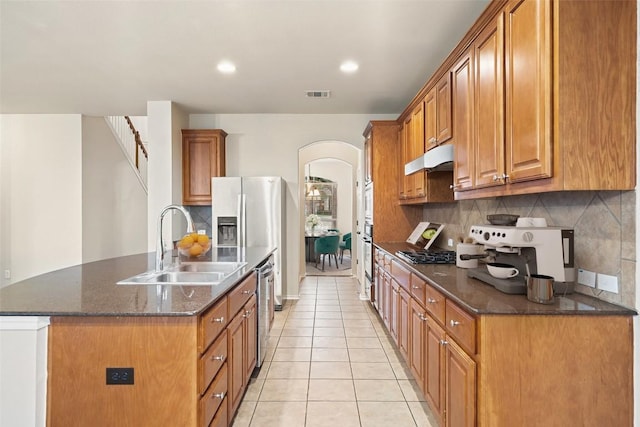 36 White Magnolia Cir, Austin, TX 78734 - kitchen with arched walkways, stainless steel appliances, backsplash, brown cabinets, and light tile patterned floors