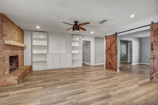 908 Hollybluff St, Austin, TX 78753 - unfurnished living room featuring a barn door, a ceiling fan, a textured ceiling, light wood-style floors, and a brick fireplace