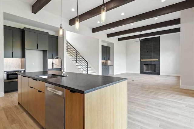 512 Cowal Dr S, Spicewood, TX 78669 - kitchen with stainless steel dishwasher, a ceiling fan, a tiled fireplace, light wood-style flooring, and beam ceiling