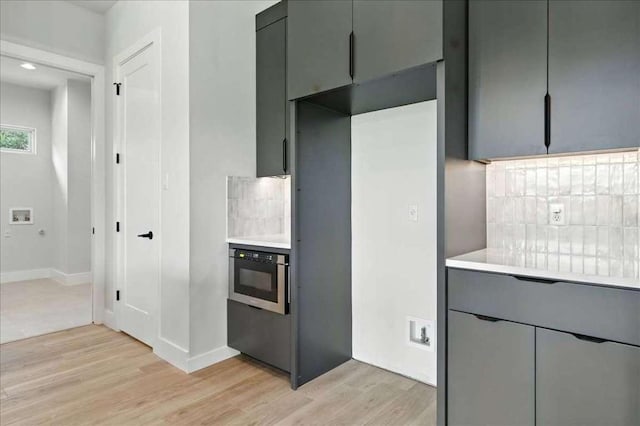 512 Cowal Dr S, Spicewood, TX 78669 - kitchen with light wood finished floors, gray cabinetry, decorative backsplash, light countertops, and wall oven