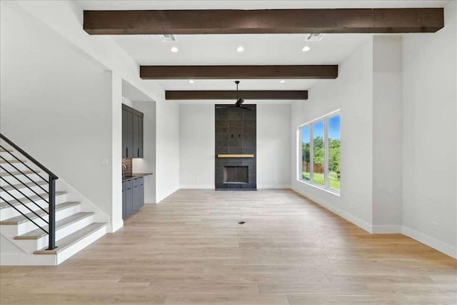 512 Cowal Dr S, Spicewood, TX 78669 - unfurnished living room featuring a ceiling fan, light wood finished floors, beamed ceiling, a fireplace, and stairway