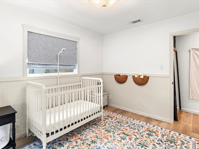 1907 Parkside Ln, Austin, TX 78745 - bedroom featuring a wainscoted wall, wood finished floors, and a crib