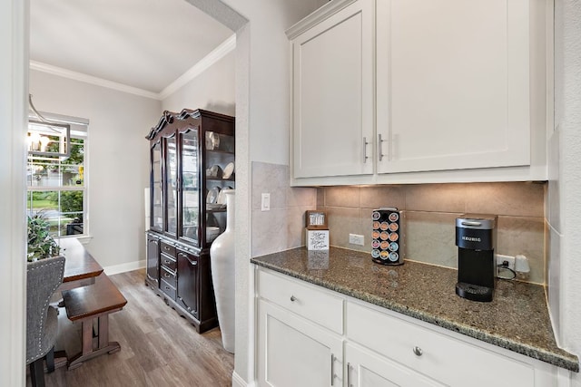 1304 Positano Pass, Leander, TX 78641 - kitchen with crown molding, light wood finished floors, dark stone counters, decorative backsplash, and white cabinets