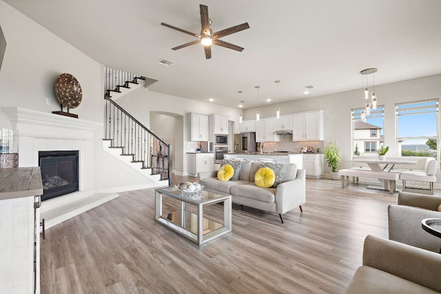 1304 Positano Pass, Leander, TX 78641 - living area featuring light wood-style flooring, stairway, a glass covered fireplace, a ceiling fan, and recessed lighting
