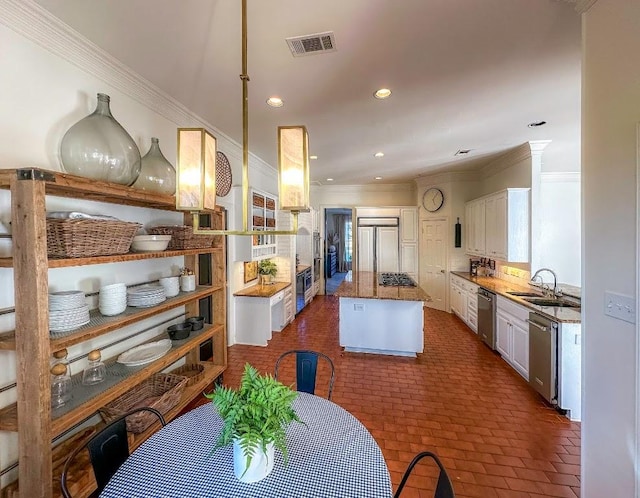 4119 Hidden Canyon Cv, Austin, TX 78746 - kitchen with stainless steel appliances, a kitchen island, ornamental molding, white cabinetry, and brick floors