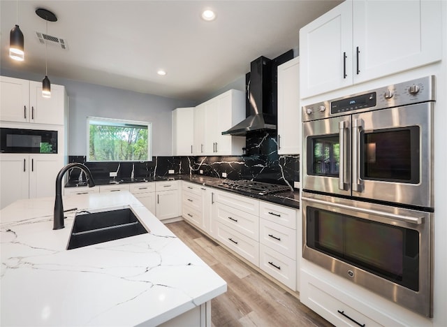 3013 Clark Ave, Lago Vista, TX 78645 - kitchen featuring appliances with stainless steel finishes, wall chimney range hood, light wood-style flooring, decorative backsplash, and light stone counters