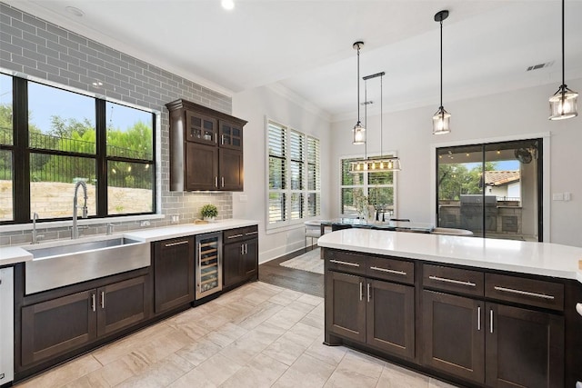 209 Ringtail Stream Dr, Lakeway, TX 78738 - kitchen featuring wine cooler, light countertops, dark brown cabinetry, pendant lighting, and ornamental molding