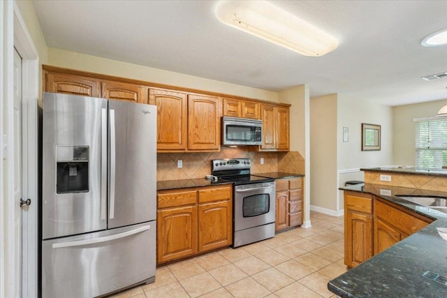 2802 Amber Forest Trl, Belton, TX 76513 - kitchen with stainless steel appliances, tasteful backsplash, light tile patterned floors, brown cabinets, and dark stone counters